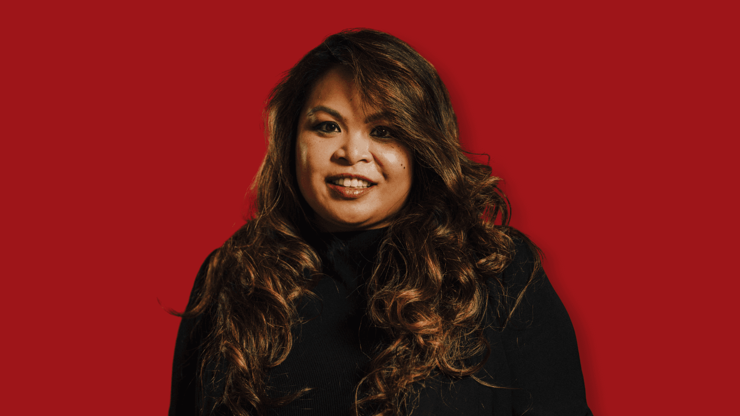 Professional woman standing in front of red background.