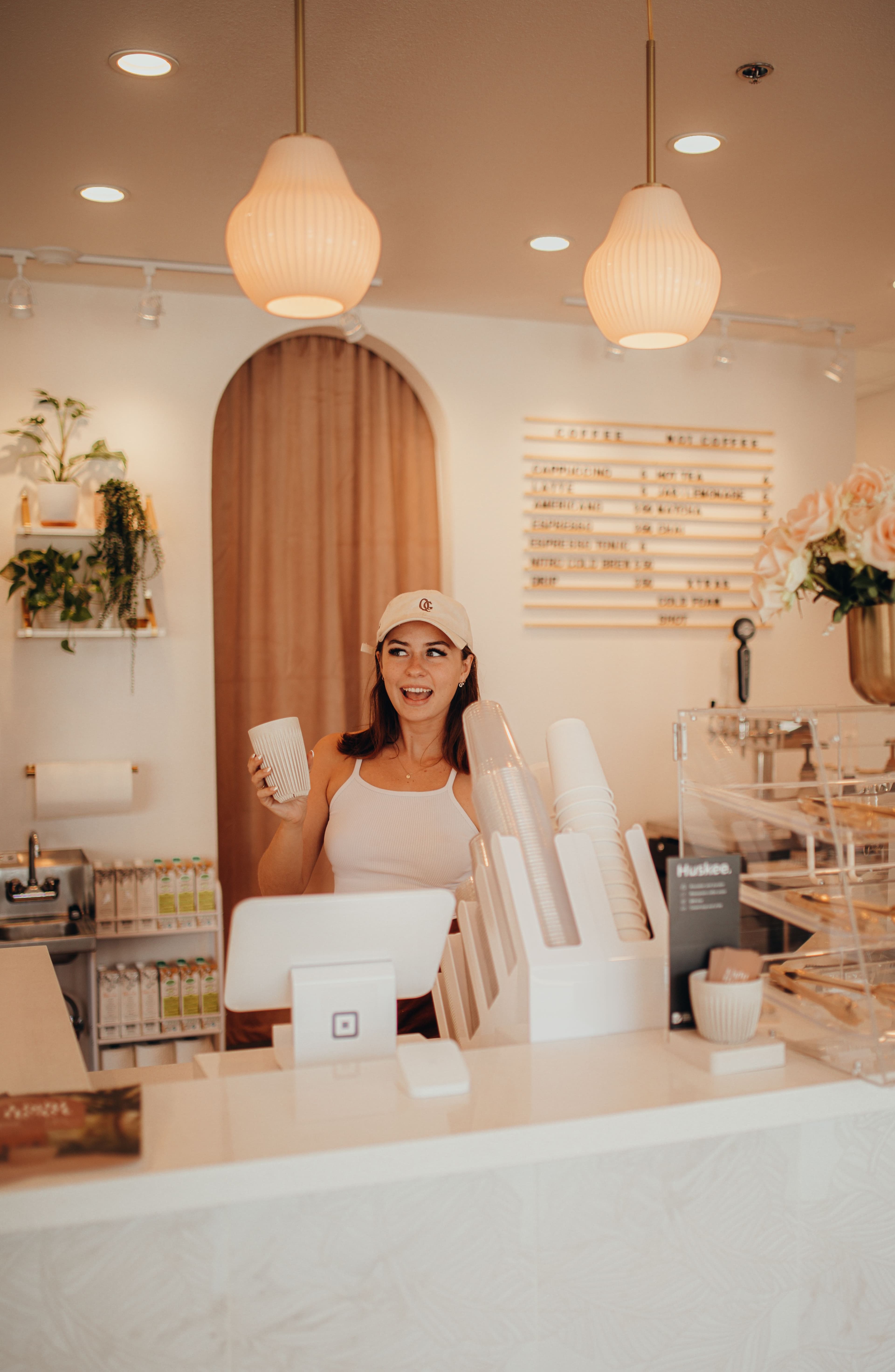 A Woman standing behind a coffee counter, holding a coffee cup with a smile on her face.